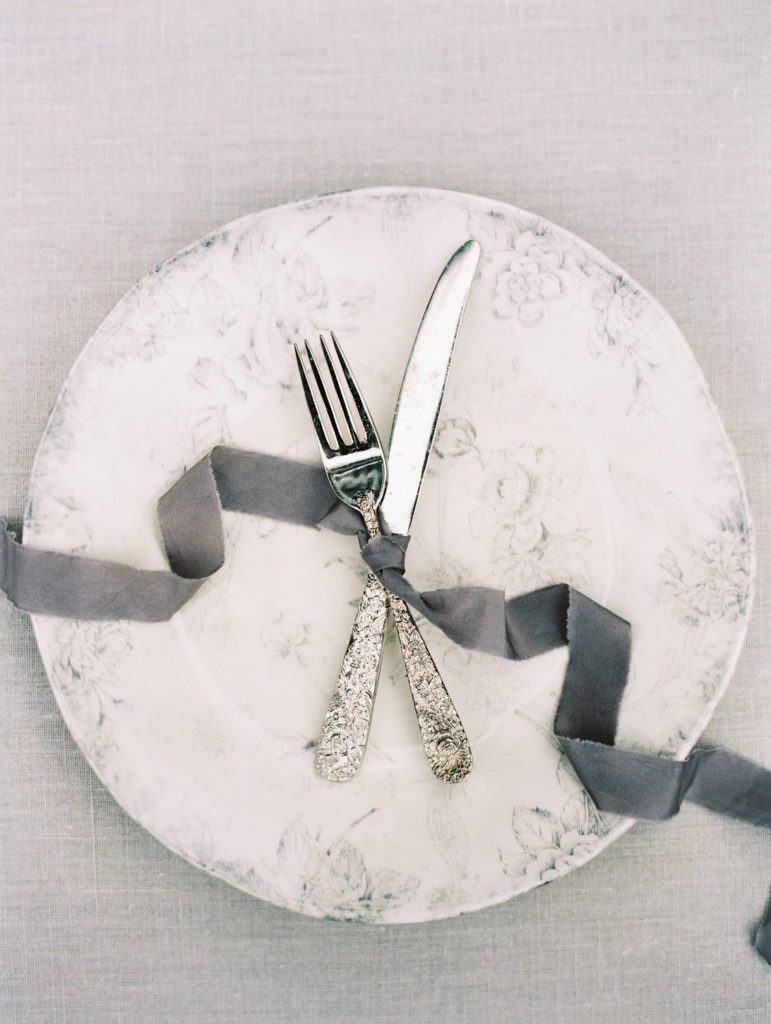 Grey floral plate styled with silver flatware and ribbon